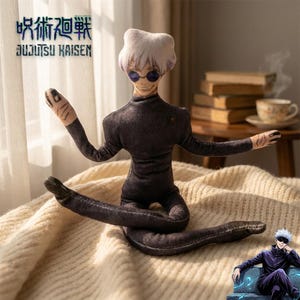 Könnte beinhalten: Plüschpuppe einer Figur aus der Anime-Serie Jujutsu Kaisen. Die Puppe sitzt mit ausgestreckten Armen. Sie hat weiße Haare, eine Sonnenbrille und trägt ein dunkelviolettes Outfit. Das Jujutsu Kaisen-Logo ist im Hintergrund zu sehen.
