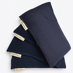 Peut inclure: Trois articles de tissu rectangulaires bleu marine sont empilés, chacun avec une surface texturée. De petites étiquettes rectangulaires avec le texte "vitalsandvibes.co" sont attachées à chaque article. Les articles sont disposés en couches, celui du dessus recouvrant partiellement les autres.