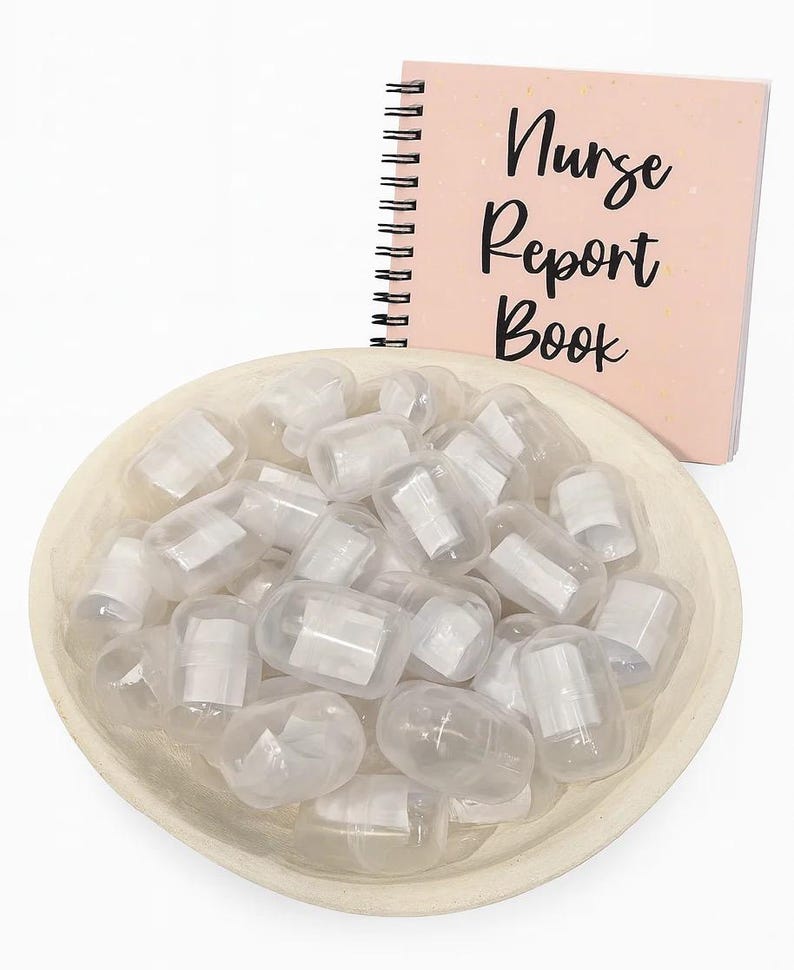 May include: A light pink spiral-bound notebook with the words "Nurse Report Book" in black script sits next to a wooden bowl filled with clear, capsule-shaped containers. The containers have white paper inserts.