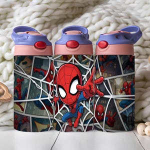 Puede incluir: Una botella de agua cilíndrica con un gráfico de estilo cómic del personaje Spider-Man en rojo y azul. La botella tiene una tapa de color morado claro con un mecanismo de apertura de botón rojo y un asa de transporte integrada.