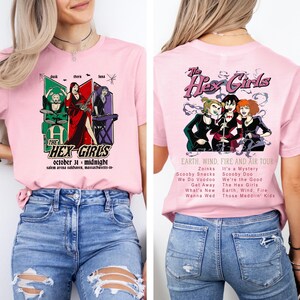 May include: Pink t-shirt featuring "The Hex Girls" graphic on the front and back. The front design includes the band's name, date, and location. The back design shows the band members with tour details. A fun, colorful tee.