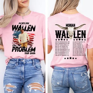 May include: Pink t-shirt featuring the text "MORGAN WALLEN" above an image of a man in front of an American flag design. The words "STILL THE PROBLEM TOUR 2026" are below. The back of the shirt has the same text and a list of tour dates.