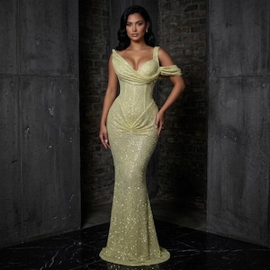 May include: A shimmering, pale yellow evening gown with a fitted bodice and a flowing mermaid skirt. The dress features a sweetheart neckline and off-the-shoulder sleeves. The fabric is covered in sequins, reflecting light.