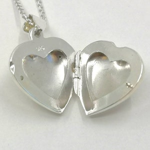 A sterling silver puffy heart locket on a silver chain. This heart necklace is on a white background. The locket is shown open and is a close up.