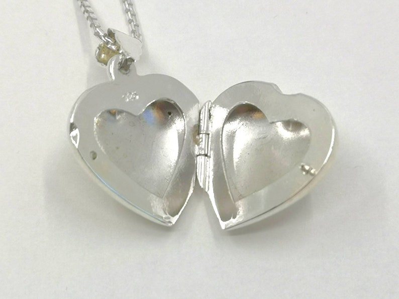 A sterling silver puffy heart locket on a silver chain. This heart necklace is on a white background. The locket is shown open and is a close up.