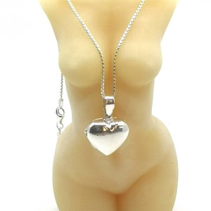 A sterling silver puffy heart locket on a silver chain. This heart necklace is on a beeswax goddess candle of a female torso nude.