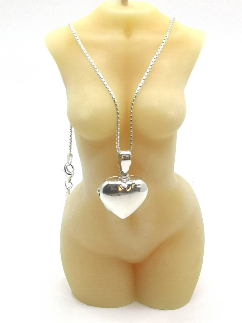 A sterling silver puffy heart locket on a silver chain. This heart necklace is on a beeswax goddess candle of a female torso nude.