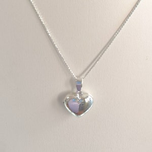 A sterling silver puffy heart locket on a silver chain. This heart necklace is on a white background. The locket is shiny and silver.