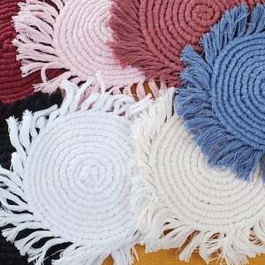May include: A collection of handmade macrame coasters in various colors, including burgundy, pink, white, black, and blue. Each coaster features a circular design with a fringed edge, perfect for protecting surfaces from drink condensation.