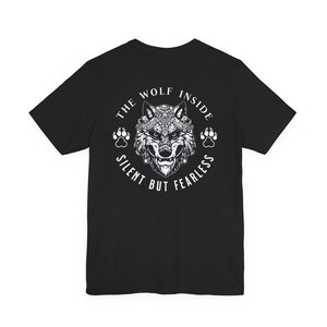 May include: Black t-shirt featuring a detailed wolf illustration with the text "THE WOLF INSIDE SILENT BUT FEARLESS" in a circular design. The wolf graphic is in white and gray, with paw prints on either side.