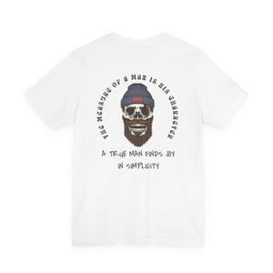 Puede incluir: Camiseta blanca con un diseño de calavera con gorro azul y barba marrón. El texto dice "THE MEASURE OF A MAN IS HIS CHARACTER" y "A TRUE MAN FINDS JOY IN SIMPLICITY".