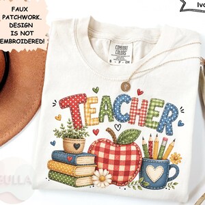 Op de afbeelding: Een ivoorkleurig t-shirt met een faux patchwork-afbeelding met het woord TEACHER in kleurrijke letters met patronen. Daaronder staan een stapel boeken, een rood geblokte appel en een blauwe mok met potloden afgebeeld. Comfort Colors label.