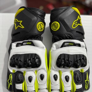Könnte beinhalten: Ein Paar schwarze, weiße und neongelbe Motorradhandschuhe. Die Handschuhe haben ein Sternlogo und den Text "GP PRO". Die Handschuhe haben eine Schutzpolsterung und sind für das Motorradfahren konzipiert.