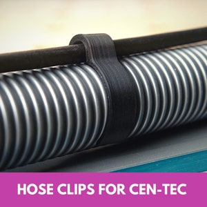 May include: A black hose clip for a vacuum cleaner hose. The clip is made of a flexible material and is designed to hold the hose in place. The text "HOSE CLIPS FOR CEN-TEC" is printed on a pink background.
