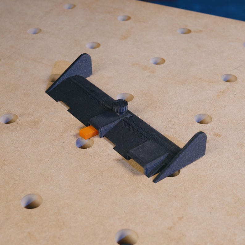 May include: A black plastic woodworking tool with an orange lever and a black knob. The tool is designed to be used on a pegboard.