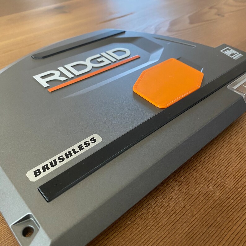 May include: A gray power tool with the word "RIDGID" in white lettering and the word "BRUSHLESS" in black lettering. The tool has an orange hexagonal button.