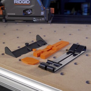 May include: A set of black and orange plastic tools for woodworking. The tools include a guide, a clamp, and a spacer. The tools are on a wooden surface.