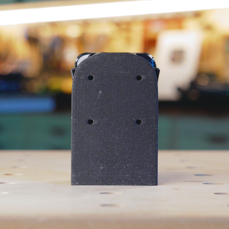 Op de afbeelding: Zwarte schuurblok met vier gaten om schuurpapier te bevestigen. Het blok is gemaakt van een getextureerd materiaal en heeft een rechthoekige vorm.
