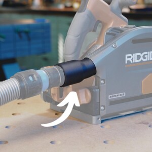 May include: A gray and black Ridgid power tool with a black dust port and a hose attached. The tool has a "Brushless" label on it. An arrow points to the dust port.