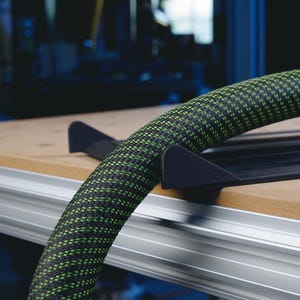 May include: A black and green hose with a black and gray hose holder. The hose is coiled and the holder is attached to a wooden surface.