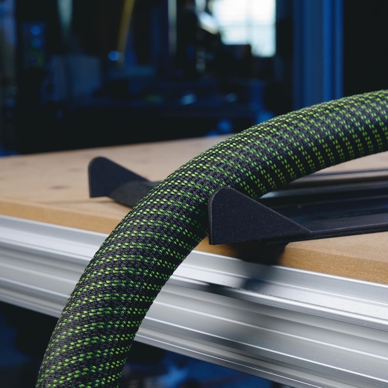May include: A black and green hose with a black and gray hose holder. The hose is coiled and the holder is attached to a wooden surface.
