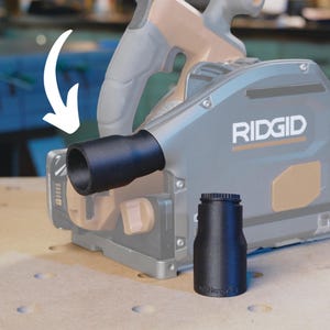 May include: A black plastic dust collection adapter for a Ridgid power tool. The adapter has a round opening and a smooth surface. The adapter is attached to the tool with a screw.
