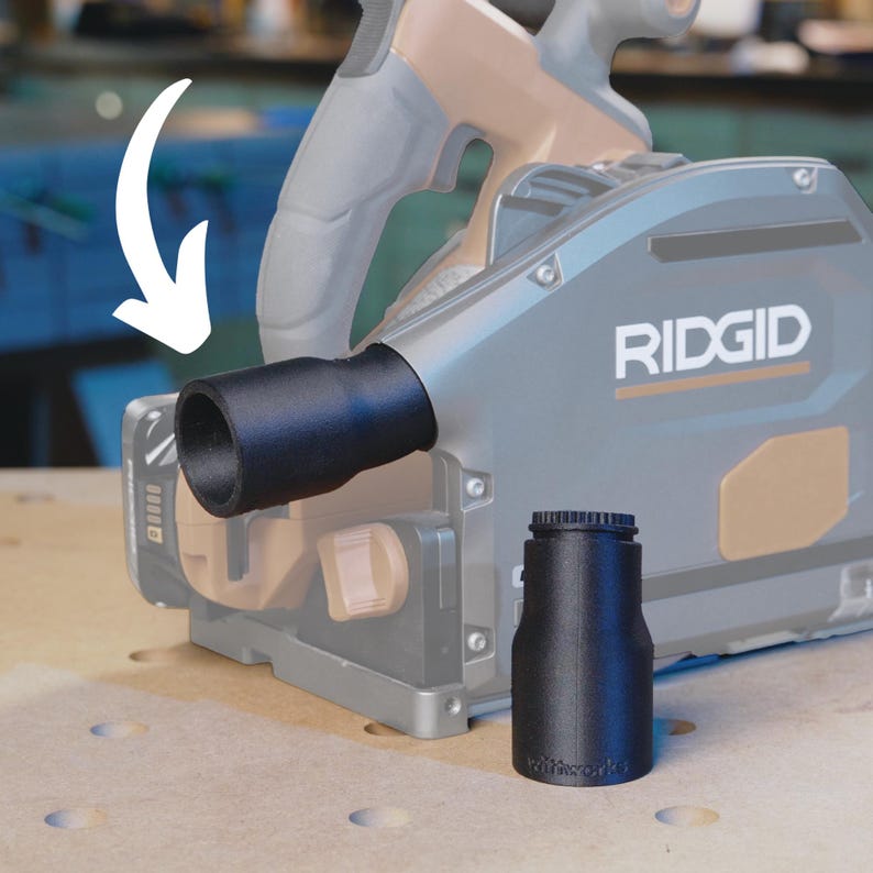 May include: A black plastic dust collection adapter for a Ridgid power tool. The adapter has a round opening and a smooth surface. The adapter is attached to the tool with a screw.