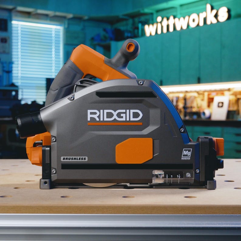 May include: A gray and orange RIDGID circular saw with a brushless motor. The saw has a clear depth gauge and a dust port. The saw is sitting on a wooden workbench.