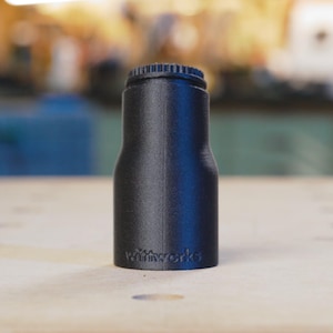 May include: A black plastic bottle stopper with a textured surface and the word "miniworks" printed on the side.
