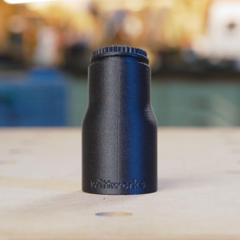 May include: A black plastic bottle stopper with a textured surface and the word "miniworks" printed on the side.