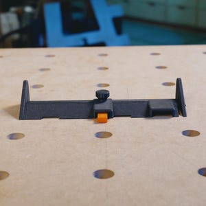 May include: A black woodworking tool with an orange adjustment knob. The tool is designed to help with woodworking projects.