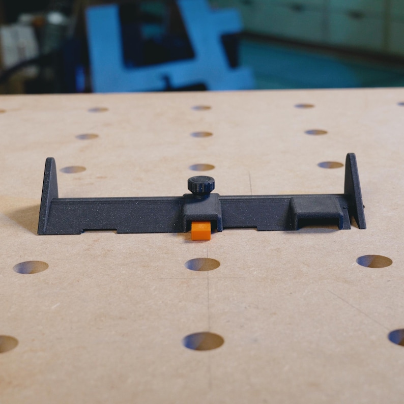 May include: A black woodworking tool with an orange adjustment knob. The tool is designed to help with woodworking projects.