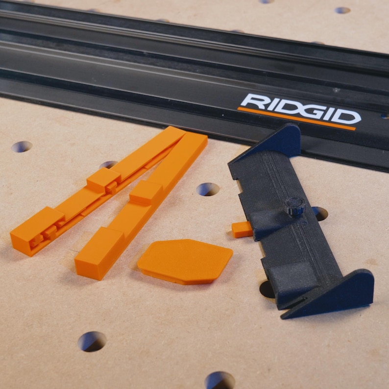 May include: A set of orange plastic woodworking jigs for a track saw system. The jigs are designed to help with cutting and aligning wood. The jigs are labeled "RIDGID".