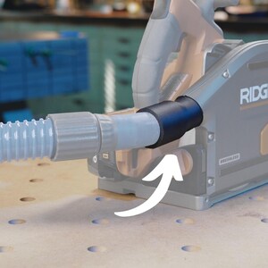May include: A gray and black power tool with a dust collection hose attached. The hose is connected to the tool with a black adapter. The tool has the word "RIDGID" printed on it.