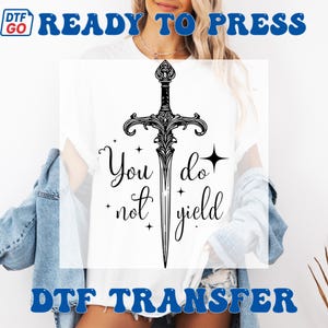 May include: White t-shirt with a black sword design and the words "You do not yield". The design includes stars and decorative elements. The words "Ready to Press" and "DTF Transfer" are also visible.