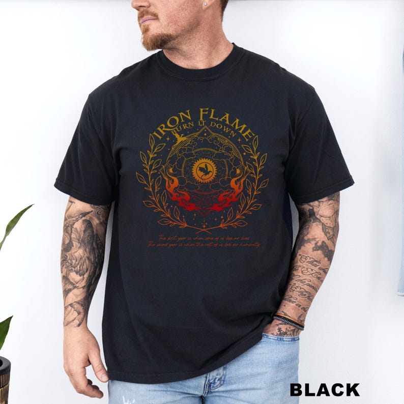 May include: Black t-shirt with a circular graphic featuring the text "IRON FLAME TURN IT DOWN" in gold. The design includes a sun, flames, and botanical elements. The shirt also has additional text at the bottom. The word "BLACK" is printed at the bottom.