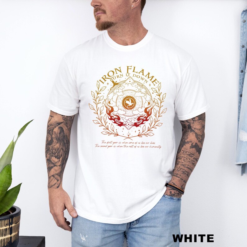 May include: White t-shirt with a circular graphic design in gold, orange, and red, featuring the text "IRON FLAME BURN IT DOWN." The design includes a central emblem and botanical elements. Below the graphic are two lines of text.