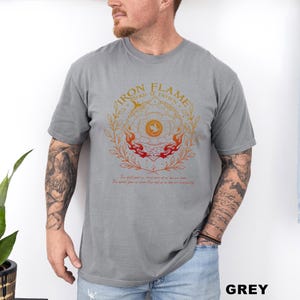 May include: Grey t-shirt with a circular graphic design in orange and red, featuring the text "IRON FLAME TURN IT DOWN". The design includes flames, a sun-like symbol, and botanical elements. Below the graphic is additional text.