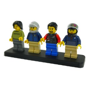 May include: Four Lego minifigures on a black base. The figures include a woman in a green shirt, a man in a blue vest and helmet, a man in a red and black vest, and a man in a blue sweater and helmet.