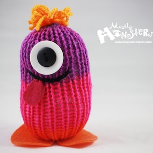 May include: A knitted purple and pink monster toy with a single white eye and a red felt tongue. The monster has orange felt hair and feet.