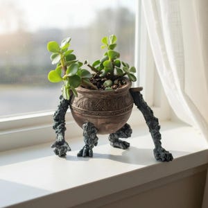 May include: A brown ceramic planter with a textured, swirling pattern around the rim, supported by three dark, gnarled, tree-like legs. A green succulent plant with rounded leaves is potted inside the vessel, which stands on a flat surface.