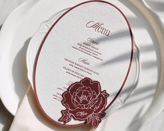 Owalna karta menu weselnego z wyciętym motywem piwonii, bordowe menu z możliwością personalizacji i imionami gości, dekoracja stołu weselnego