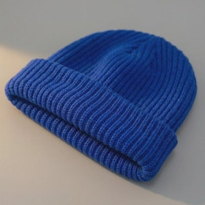 May include: A vibrant blue beanie hat with a folded brim. The hat is made of a ribbed knit fabric, offering a textured appearance. The bright blue color is consistent throughout the hat, creating a simple yet stylish accessory.