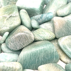 May include: A collection of smooth, light green amazonite tumbled stones. The stones are various sizes and shapes, with a natural, polished finish.