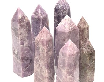May include: A group of eight purple lepidolite crystal points, some with a more lavender hue, arranged on a white background. The points are various sizes and shapes, with some being more slender than others.