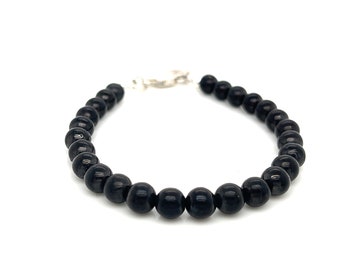 Puede incluir: Una pulsera de cuentas compuesta por una sola hilera de piedras redondas y pulidas en tonos azul oscuro y negro. Las cuentas son de tamaño uniforme y están dispuestas en forma circular, unidas por un cierre de mosquetón metálico plateado.