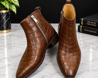 May include: A pair of brown ankle boots featuring a textured crocodile skin pattern, a pointed toe, a silver-toned side zipper closure, a pull tab at the heel, and a low block heel. The interior lining is a light tan color.