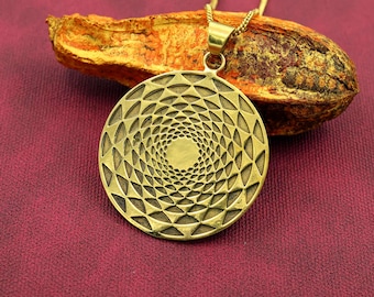 Könnte beinhalten: Eine goldfarbene Halskette mit Anhänger und einem kreisförmigen Design mit einem Spiralmuster. Der Anhänger hängt an einer zarten Kette. Die Halskette liegt auf einer rot-violetten Oberfläche, mit einem Stück getrockneter orange-brauner Rinde im Hintergrund.
