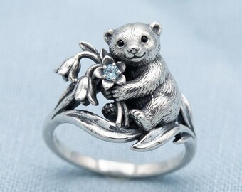 Anillo con diseño de flor de nutria y piedra azul plateada, banda decorativa con motivos de animales y naturaleza.