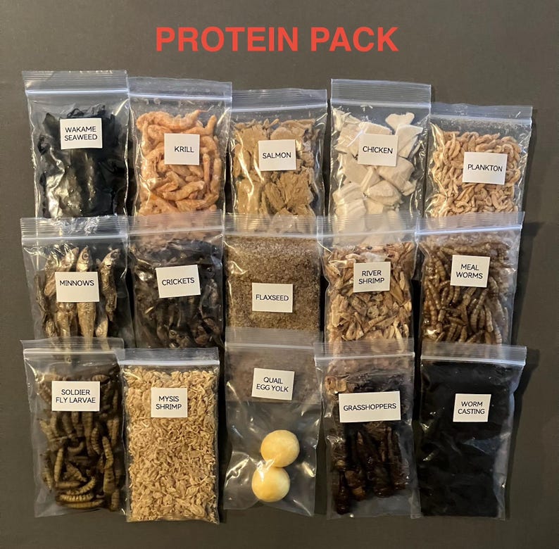 May include: A collection of clear plastic bags filled with various protein sources, including wakame seaweed, krill, salmon, chicken, and plankton. The bags are labeled with white text. The words "PROTEIN PACK" are displayed in red at the top.